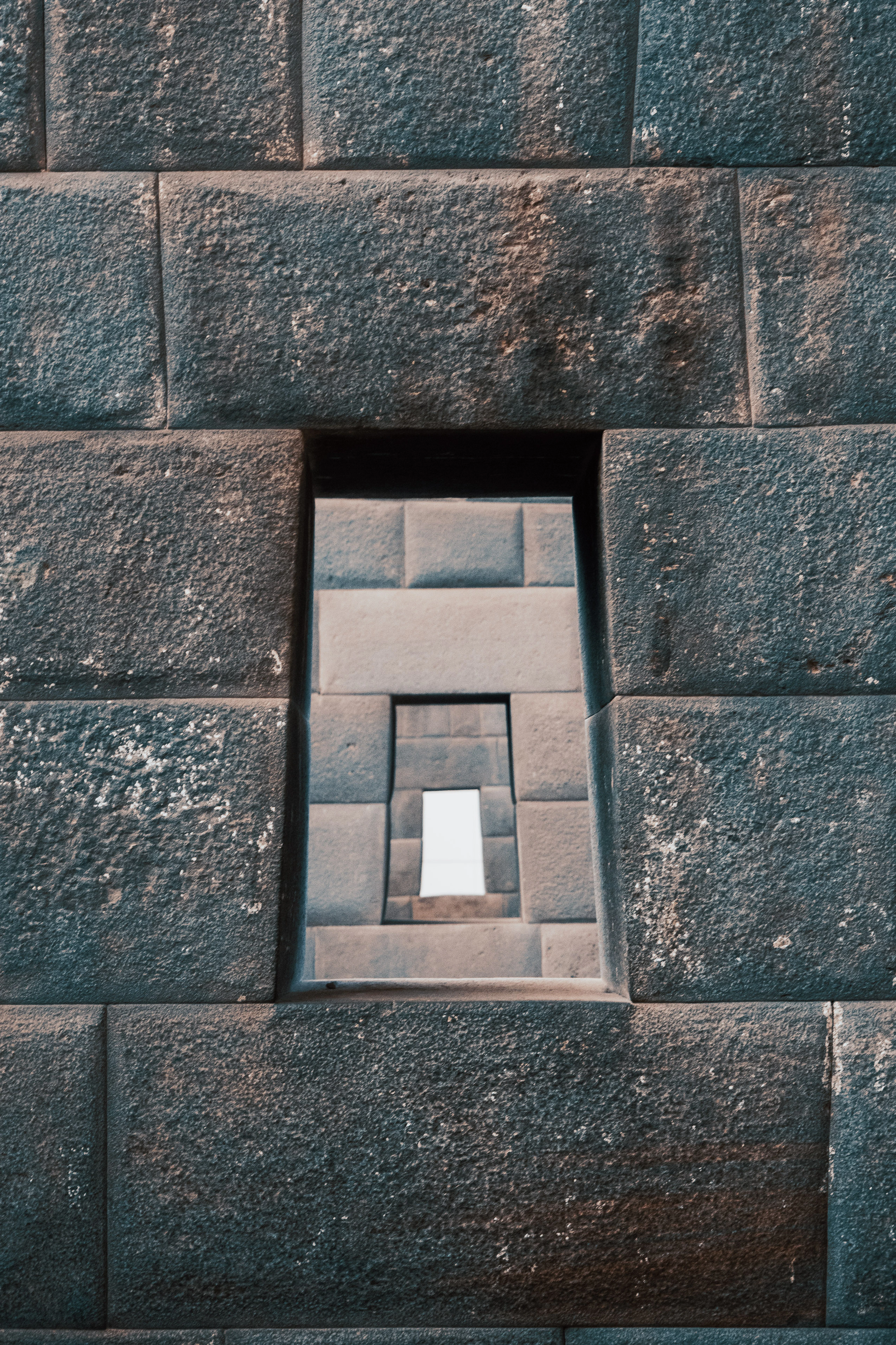 Trapezoidal Inca windows lined up through the mortarless stone walls of the Qorikancha in Cusco, each frame smaller than the last so a slot of white daylight shows at the far end.