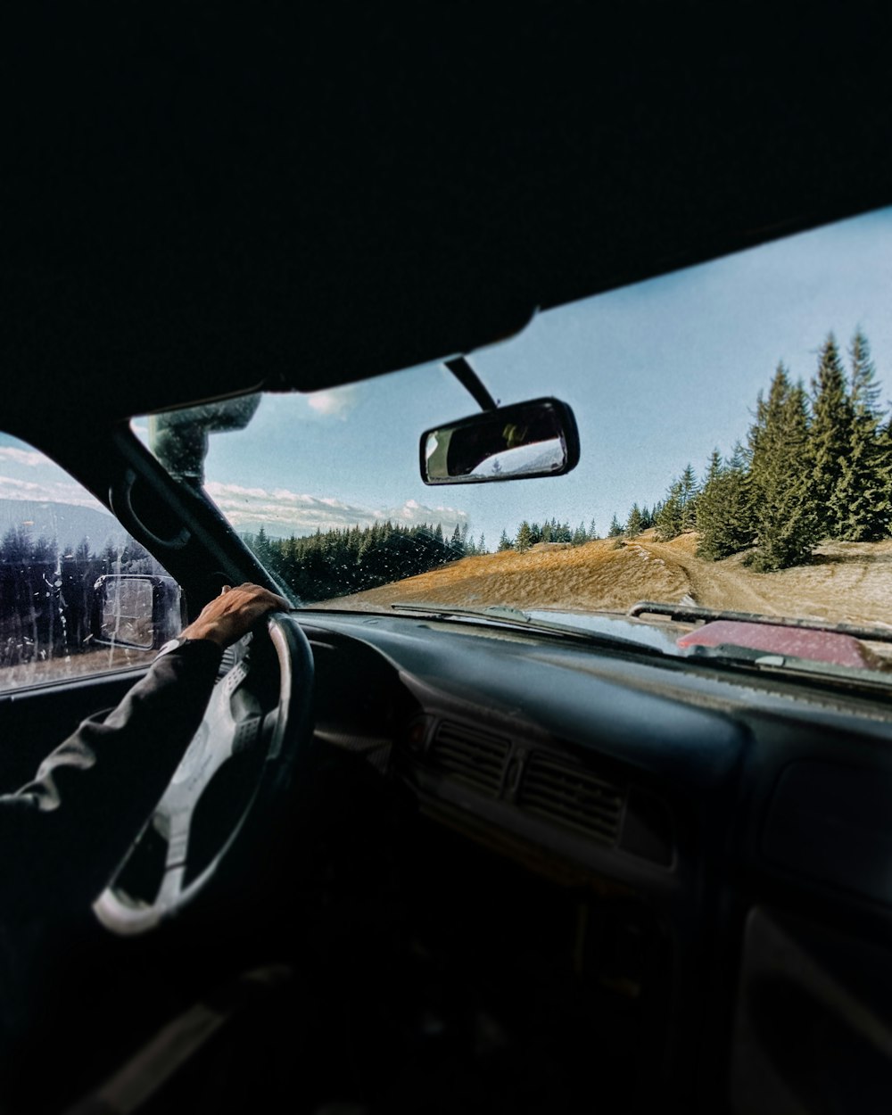 a man driving a car down a road next to a forest