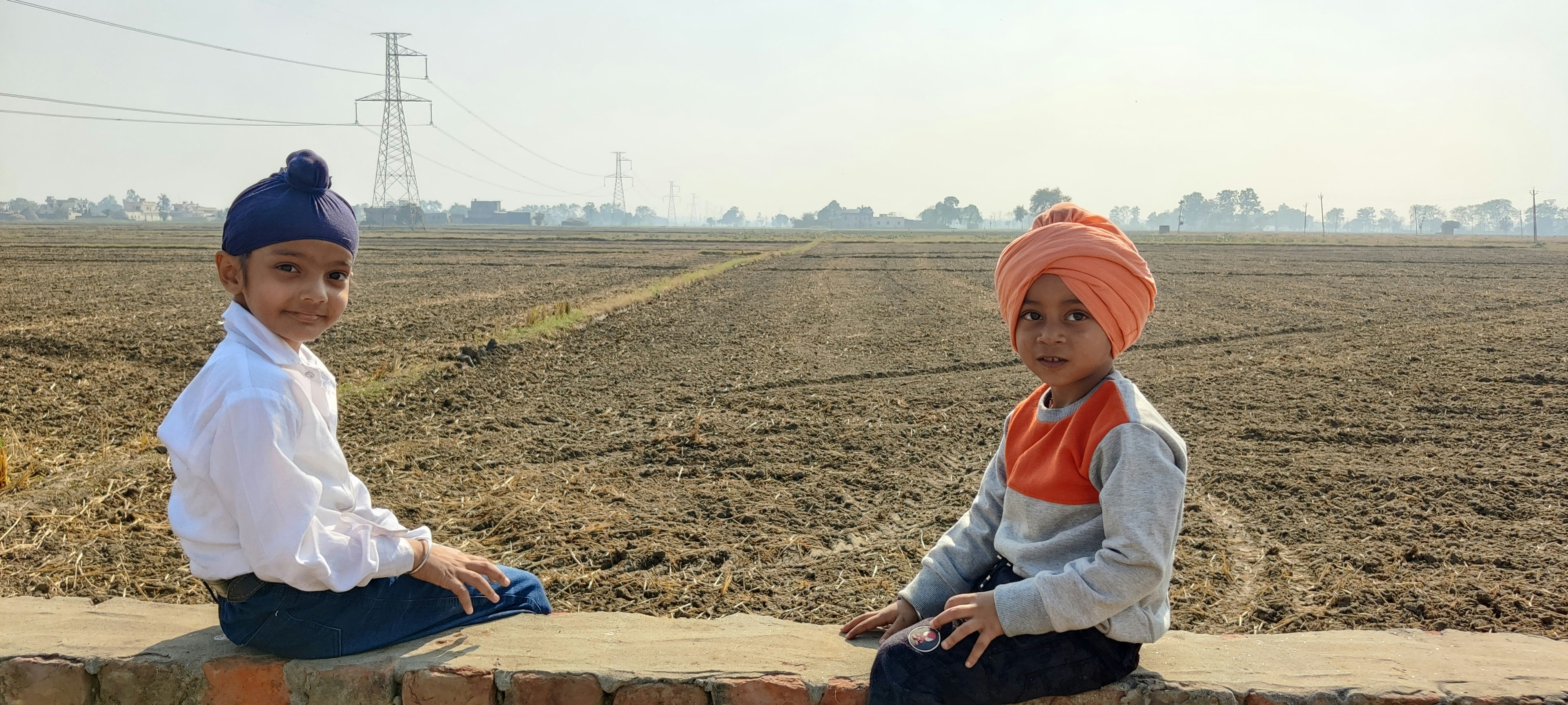 two children sitting on a brick wall in a field