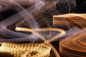 A dynamic display of light trails creating abstract and fluid patterns against a dark background. Curved and intersecting lines in colors like orange, white, and blue seem to move in waves, suggesting motion and energy.