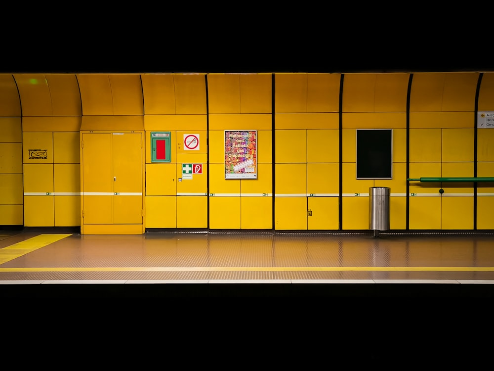 a train station with a yellow wall and a bench