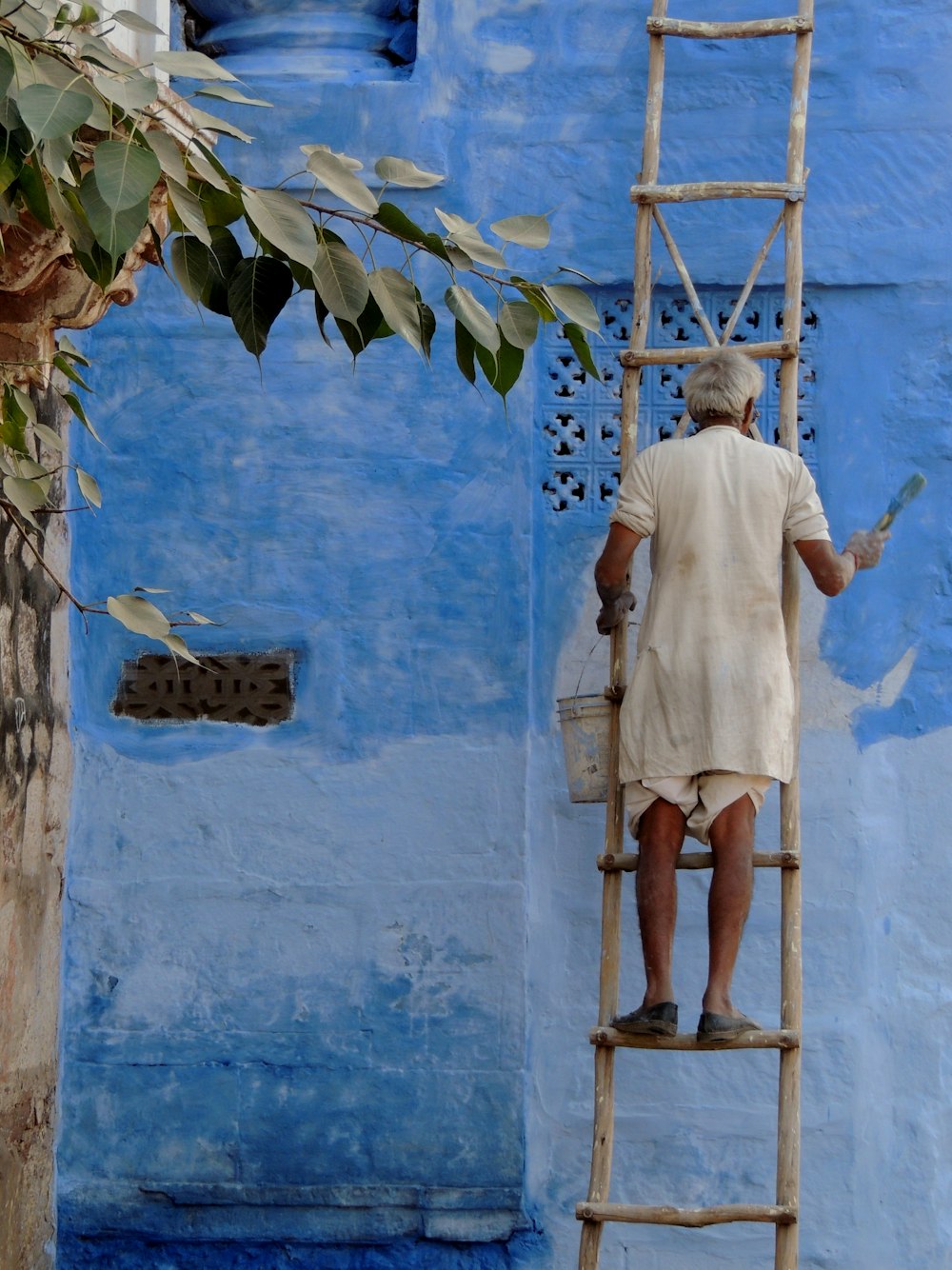 a man on a ladder painting a blue wall