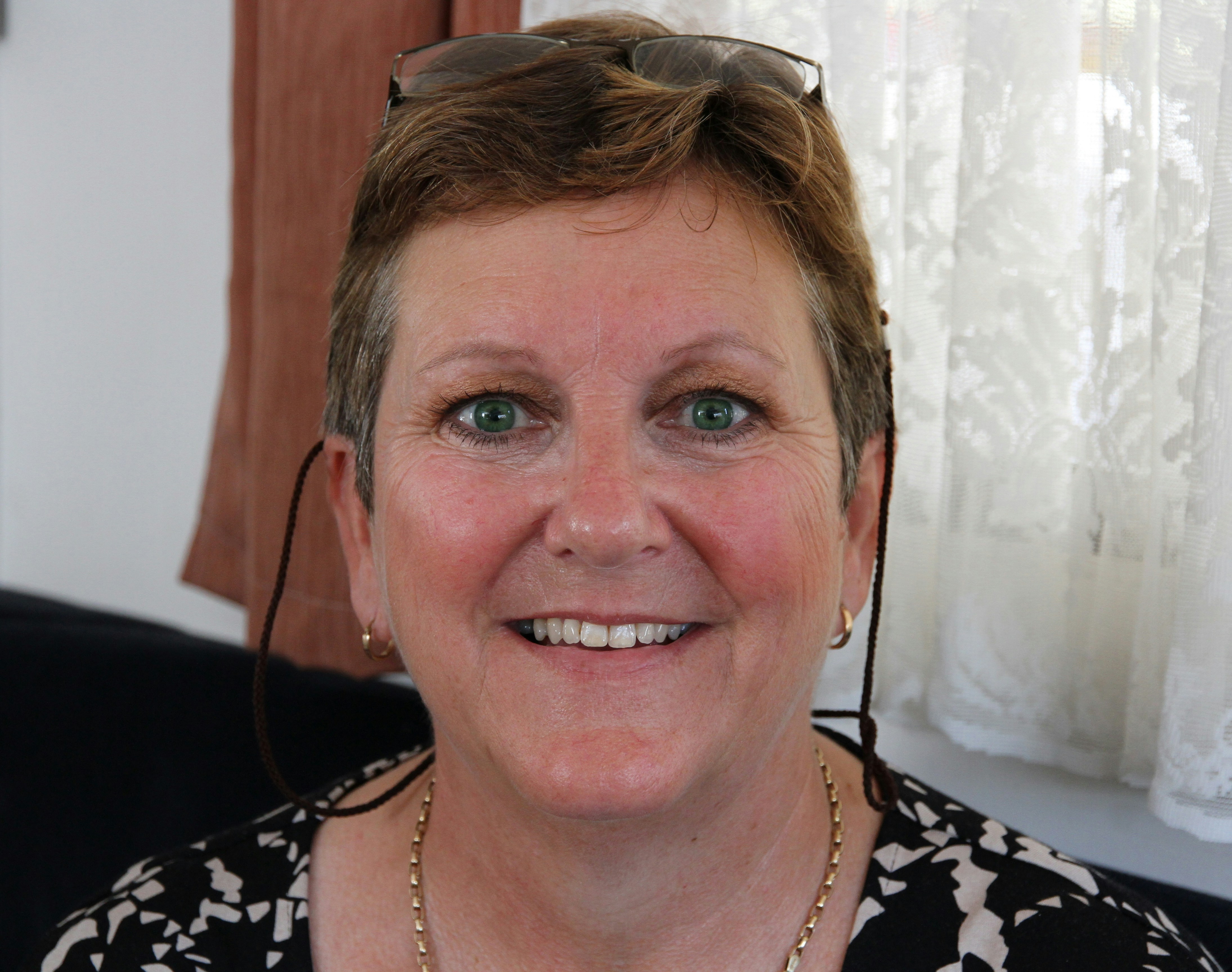 A middle-aged woman smiling warmly in a cozy, well-ventilated living room.