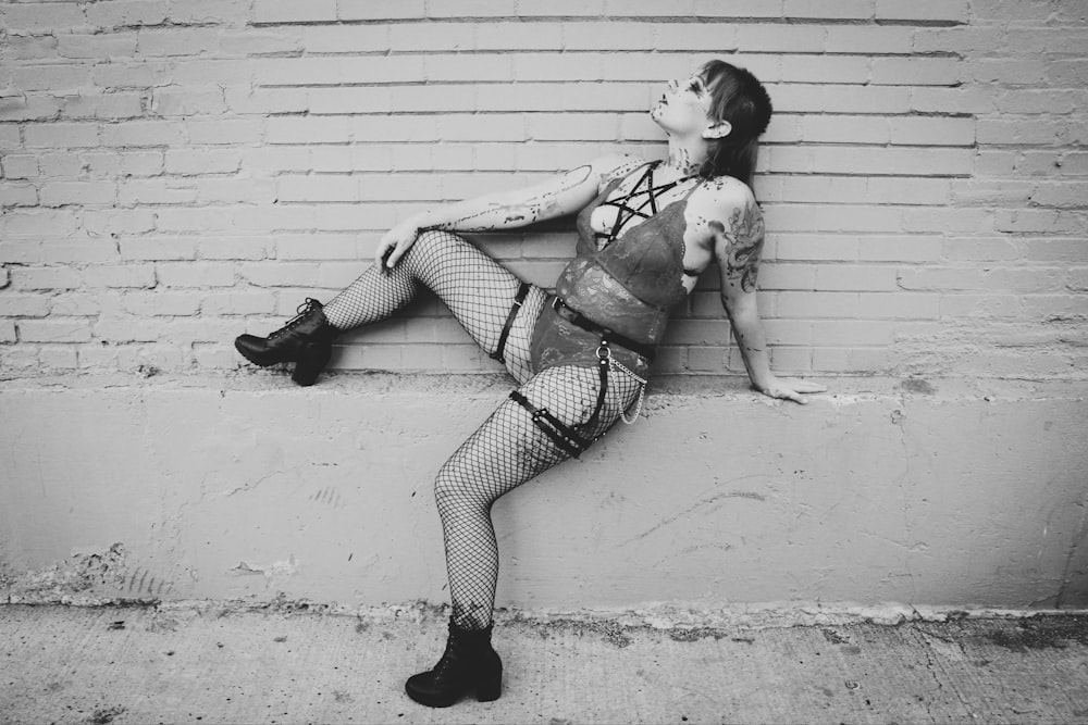 a woman in fishnet stockings leaning against a brick wall