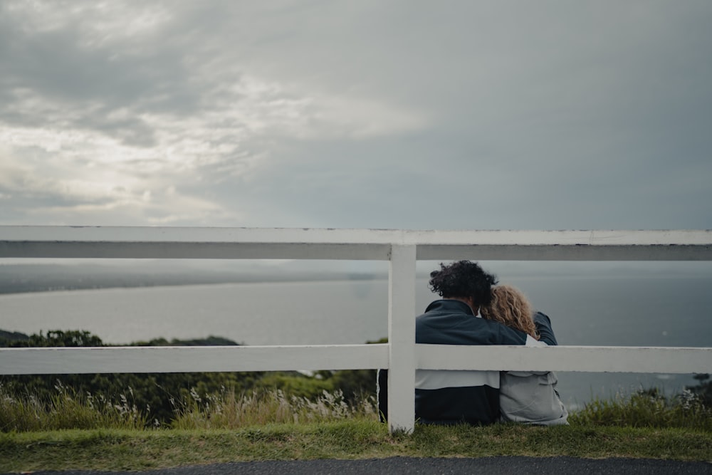 a man and a woman sitting on a bench looking at the ocean