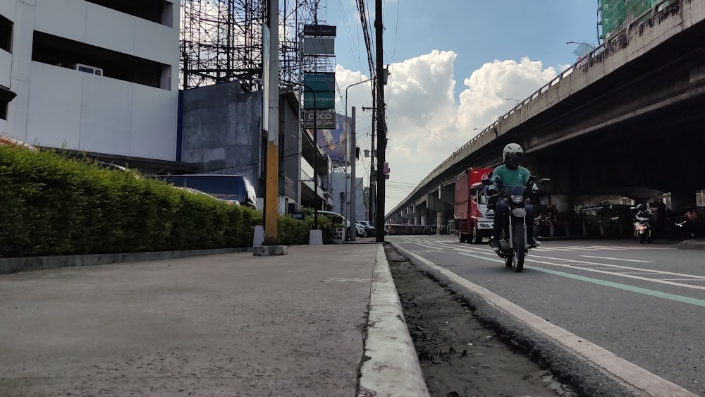 a man riding a motorcycle down a street under a bridge