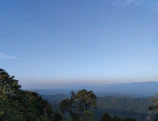 A serene mountain landscape under a clear blue sky with lush green trees.