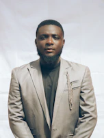 A model wearing a sleek, tailored jacket standing against a soft gray backdrop.
