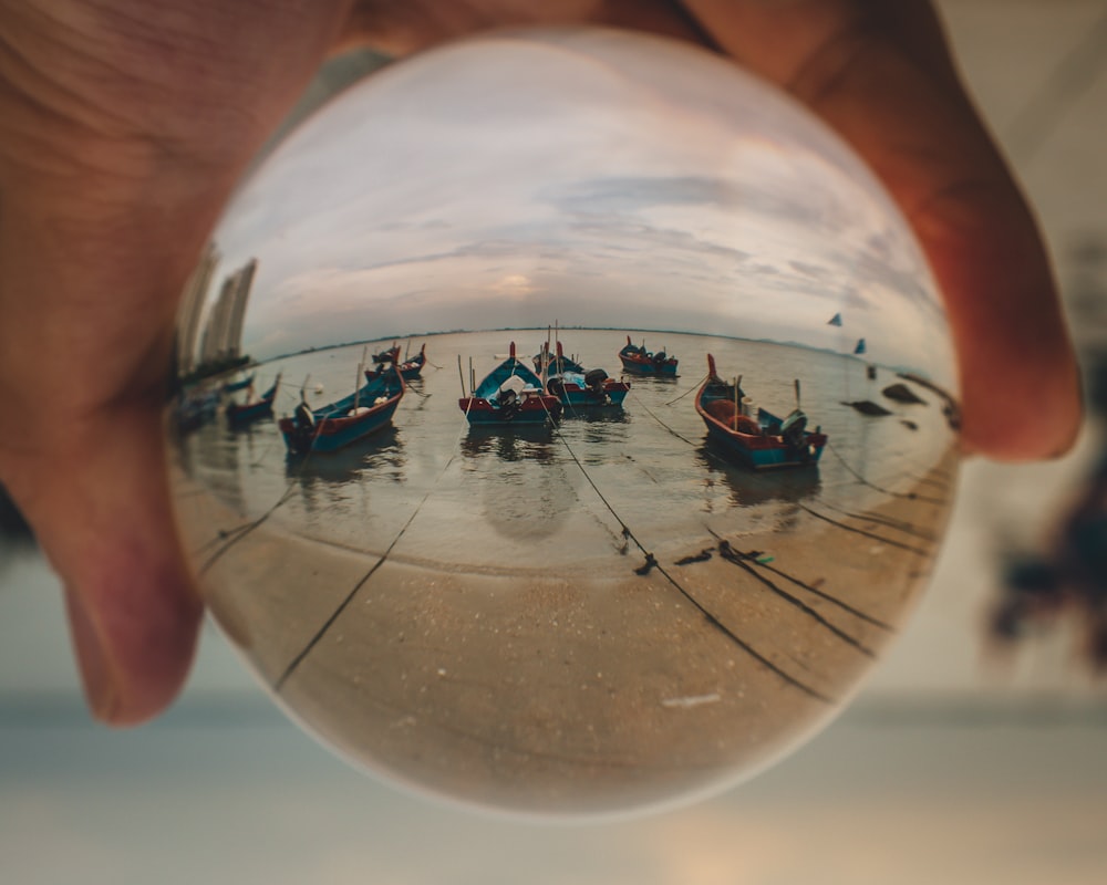 a hand holding a glass ball with a reflection of boats in it