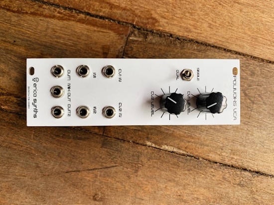 A compact electronic device with multiple input and output jacks arranged in two rows. The top row has jacks labeled CV IN, IN1, and CV2 IN, while the bottom row includes OUT MIX, OUT1, and OUT2. Two black knobs labeled CV2 LEVEL and CV1 LEVEL are situated to the right of the jacks, beside a small toggle switch for selecting 'DUAL' or 'SINGLE'. The device has a sleek white faceplate with black text, and rests on a wooden surface.