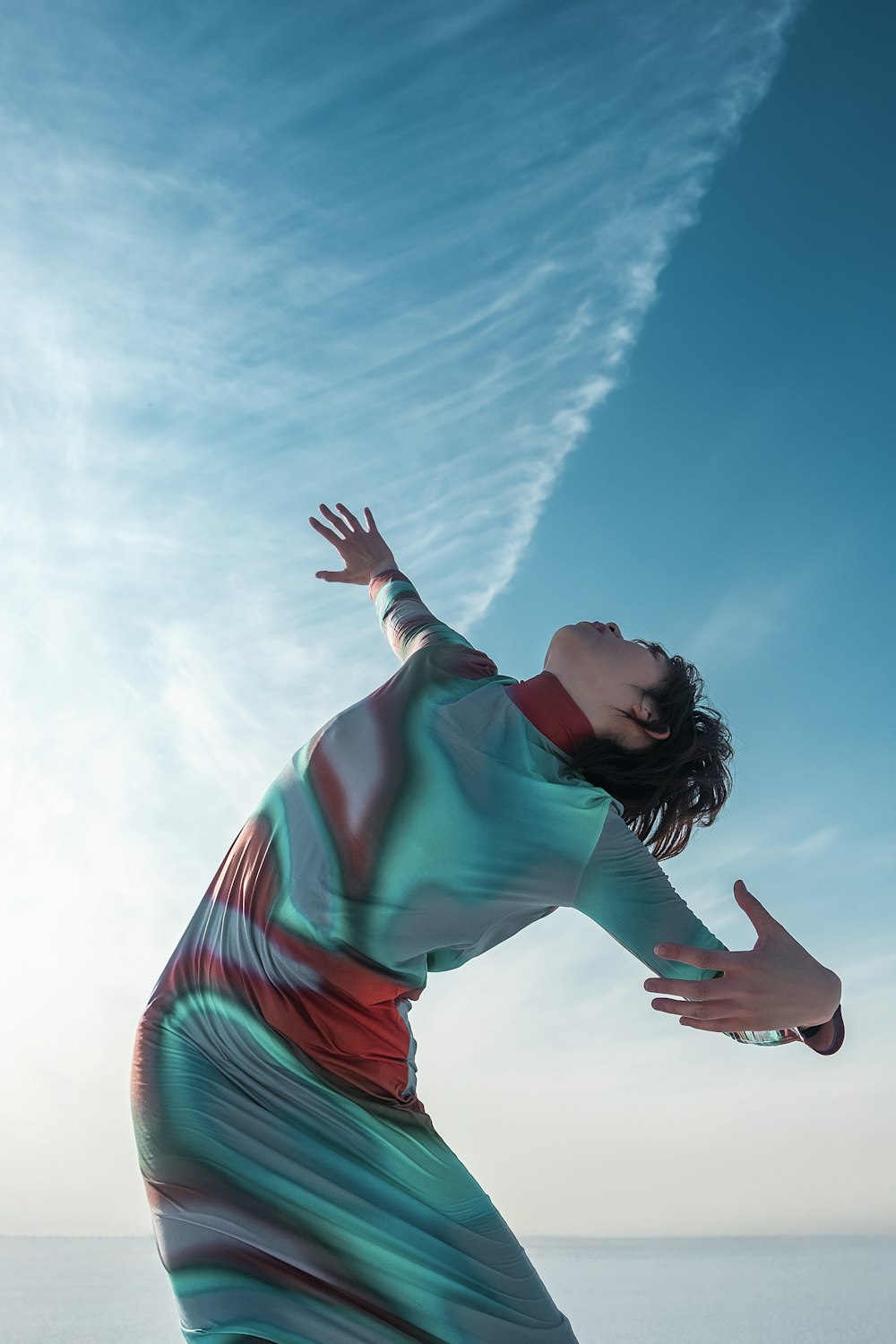 a woman in a long dress reaching up to catch a frisbee