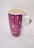 A ceramic mug with a tall, cylindrical shape and a handle on one side. The mug features a purple background adorned with yellow decorative elements, including stars, hearts, and circles arranged in vertical lines.