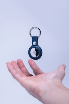 A hand is positioned palm up against a light background, appearing to support or catch a floating keychain with an electronic tracker attached.
