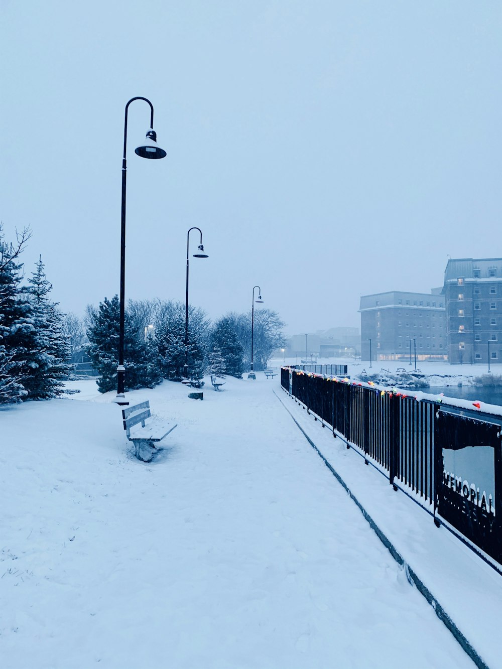 a snowy street with a bench and street lights