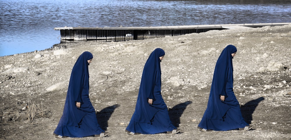Un grupo de mujeres con velos azules de pie frente a un cuerpo de agua
