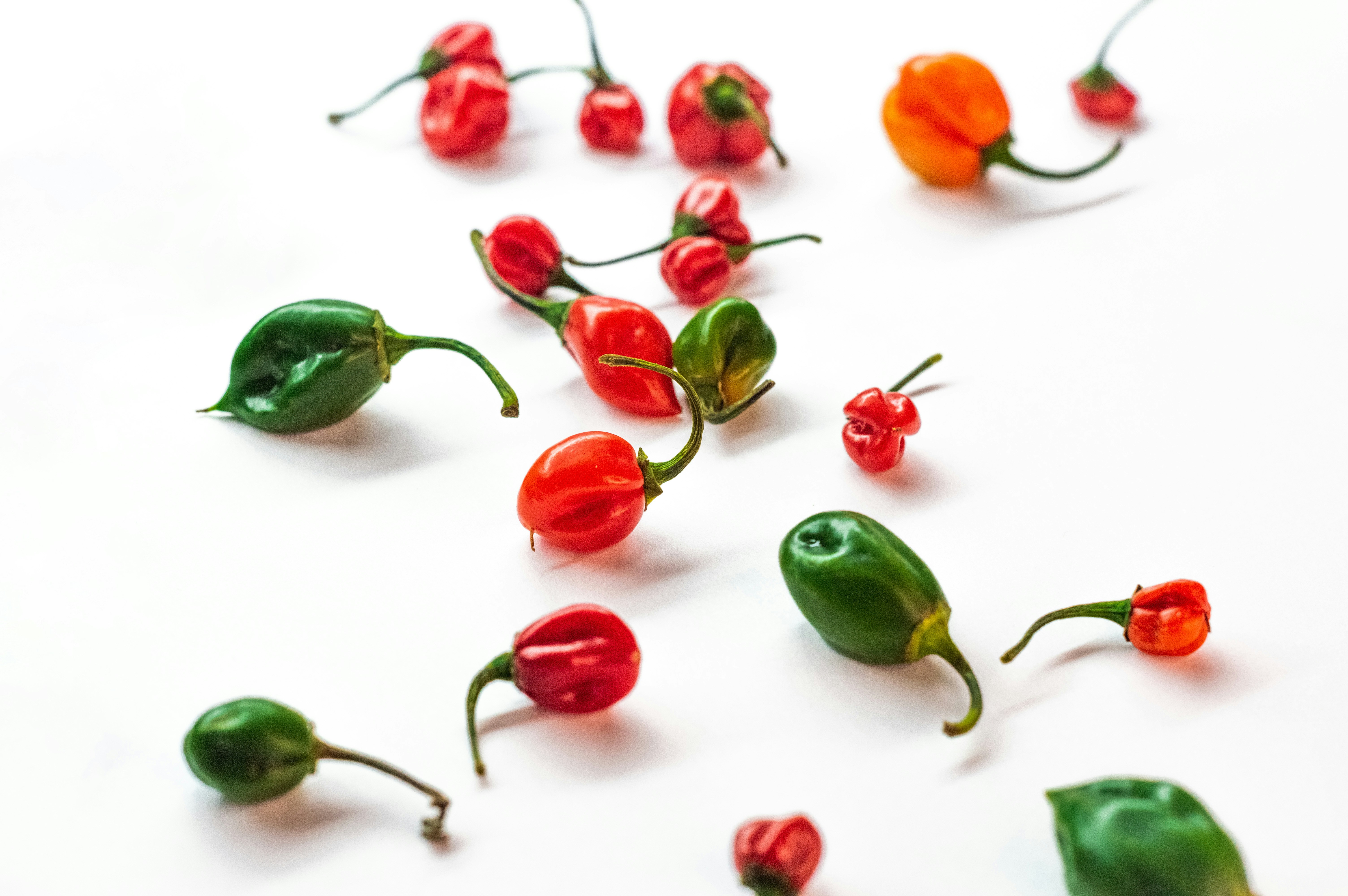 a group of red and green peppers on a white surface, Habanero chili peppers falling on isolated white background e mexico, Naga jolokia (the hottest chili peppers in the world)