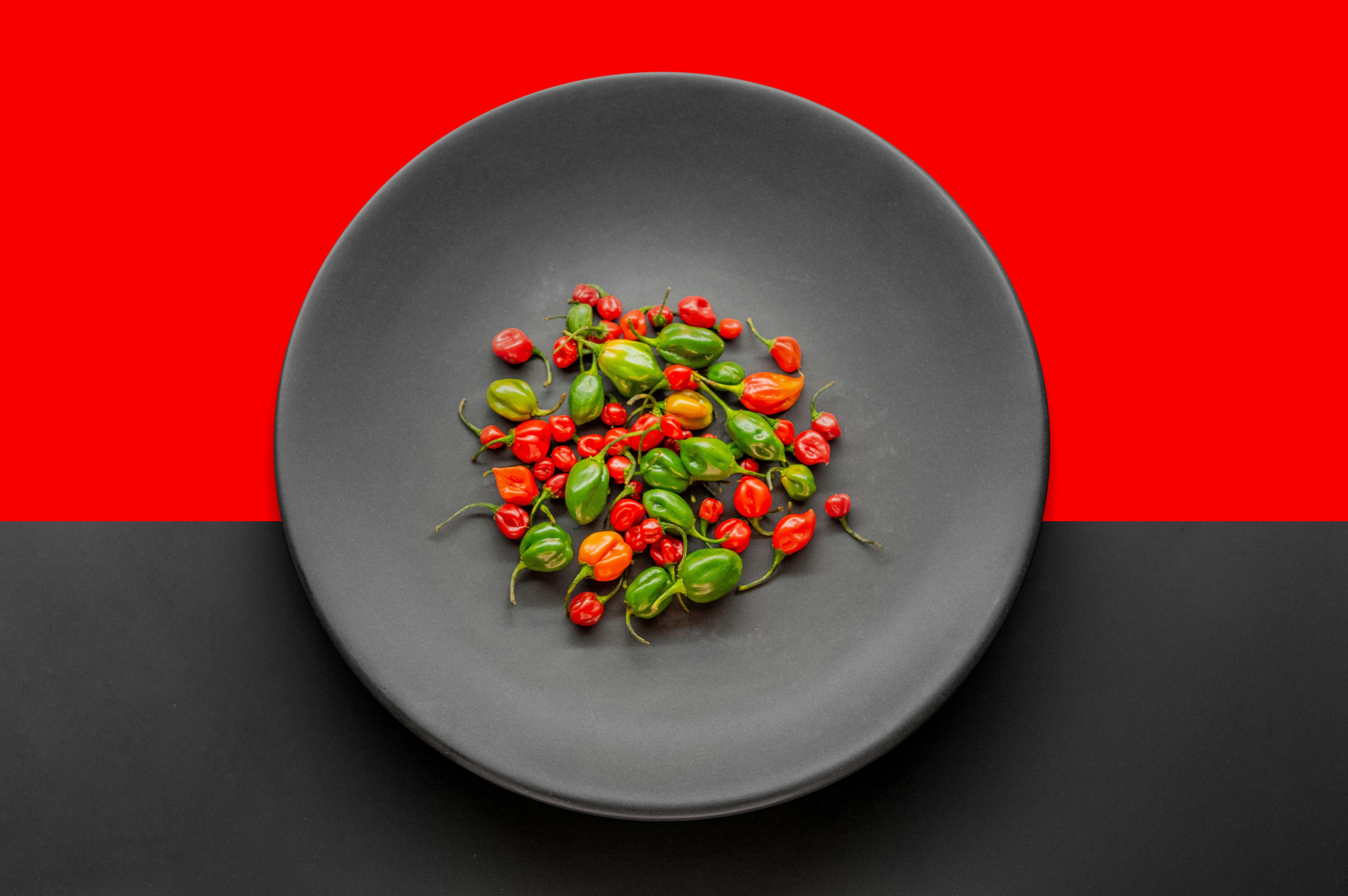 a black plate topped with green and red peppers, Habanero chili peppers falling on isolated white background e mexico, Naga jolokia (the hottest chili peppers in the world)