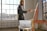A person stands by an easel, painting in a well-lit studio with large windows. The interior is modern, featuring white brick walls and a wooden floor. Natural light streams through the windows, creating a warm and inviting atmosphere. A tablet is placed on a small round table nearby.