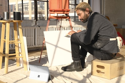 a man sitting on top of a box next to a easel
