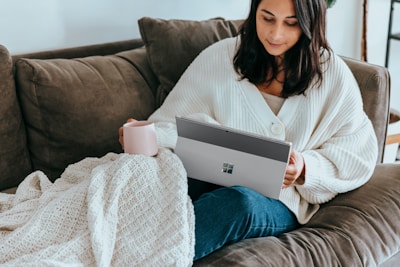A shopper comfortably browsing products on a laptop at home with a cup of tea nearby.