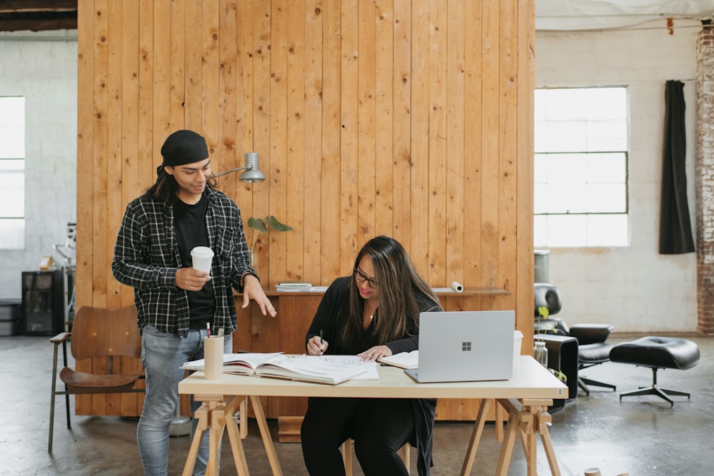 a man standing next to a woman working on a laptop