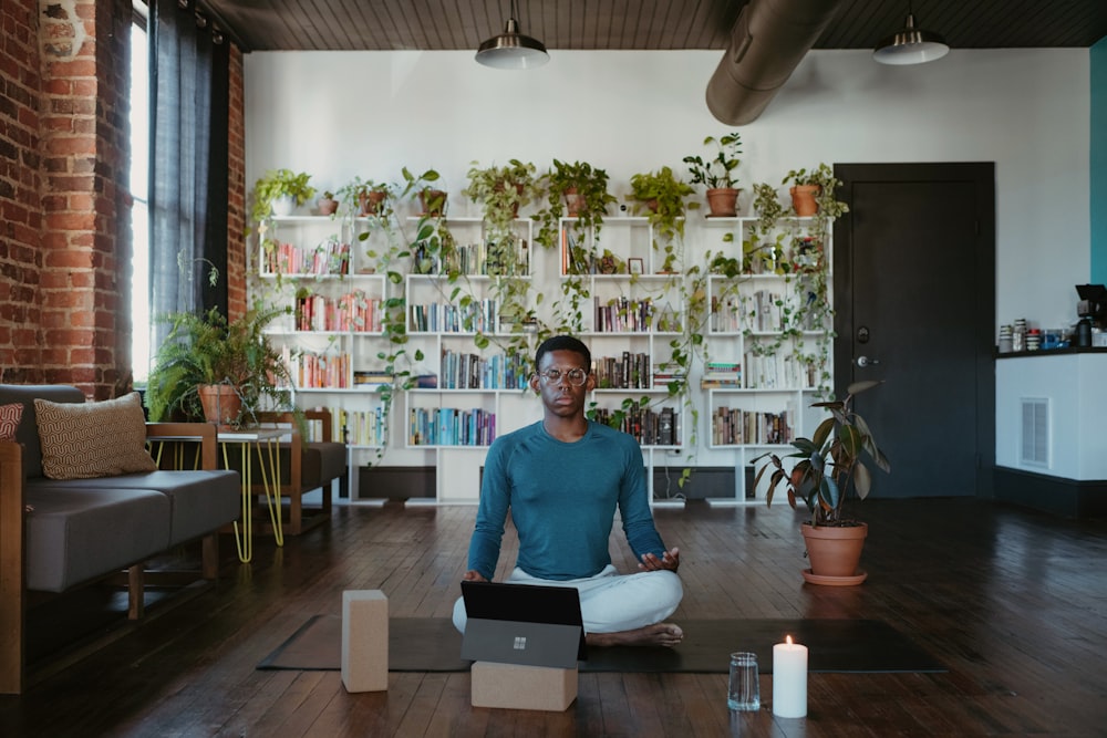 Un hombre sentado en una esterilla de yoga con una computadora portátil frente a él