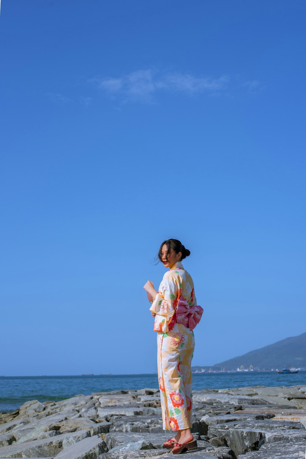 a woman in a kimono standing on rocks by the ocean