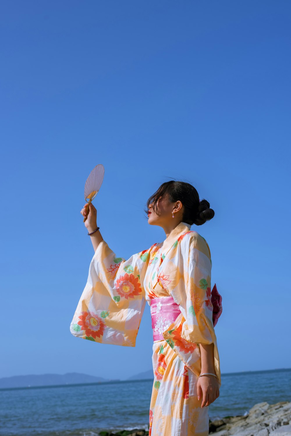 a woman standing on a beach holding a fan
