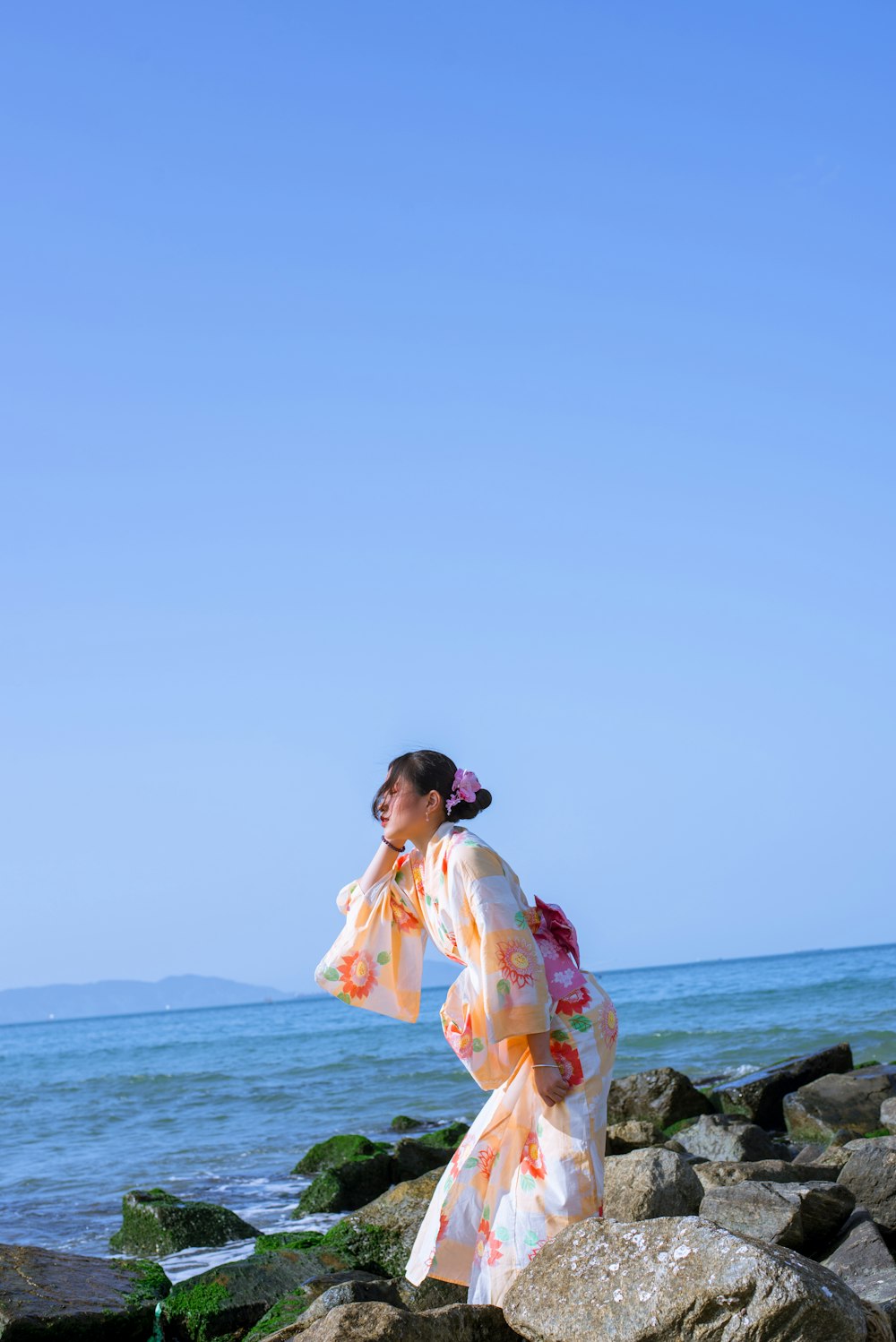 a woman in a kimono standing on rocks near the ocean