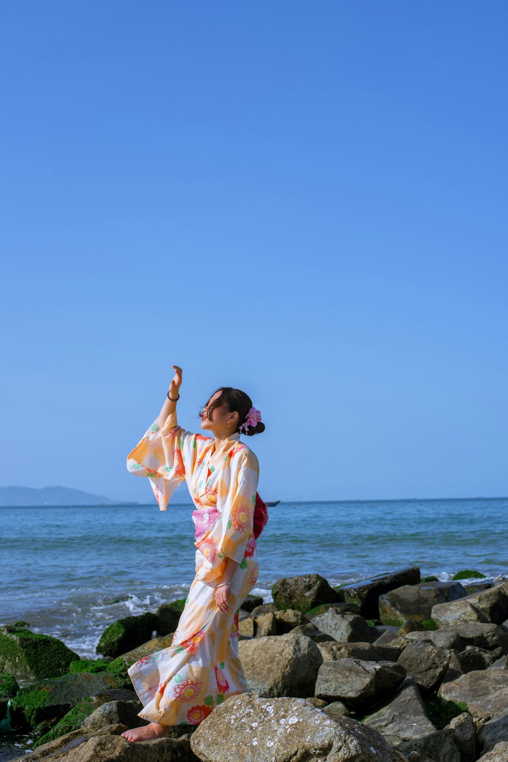 a woman in a kimono standing on rocks by the ocean