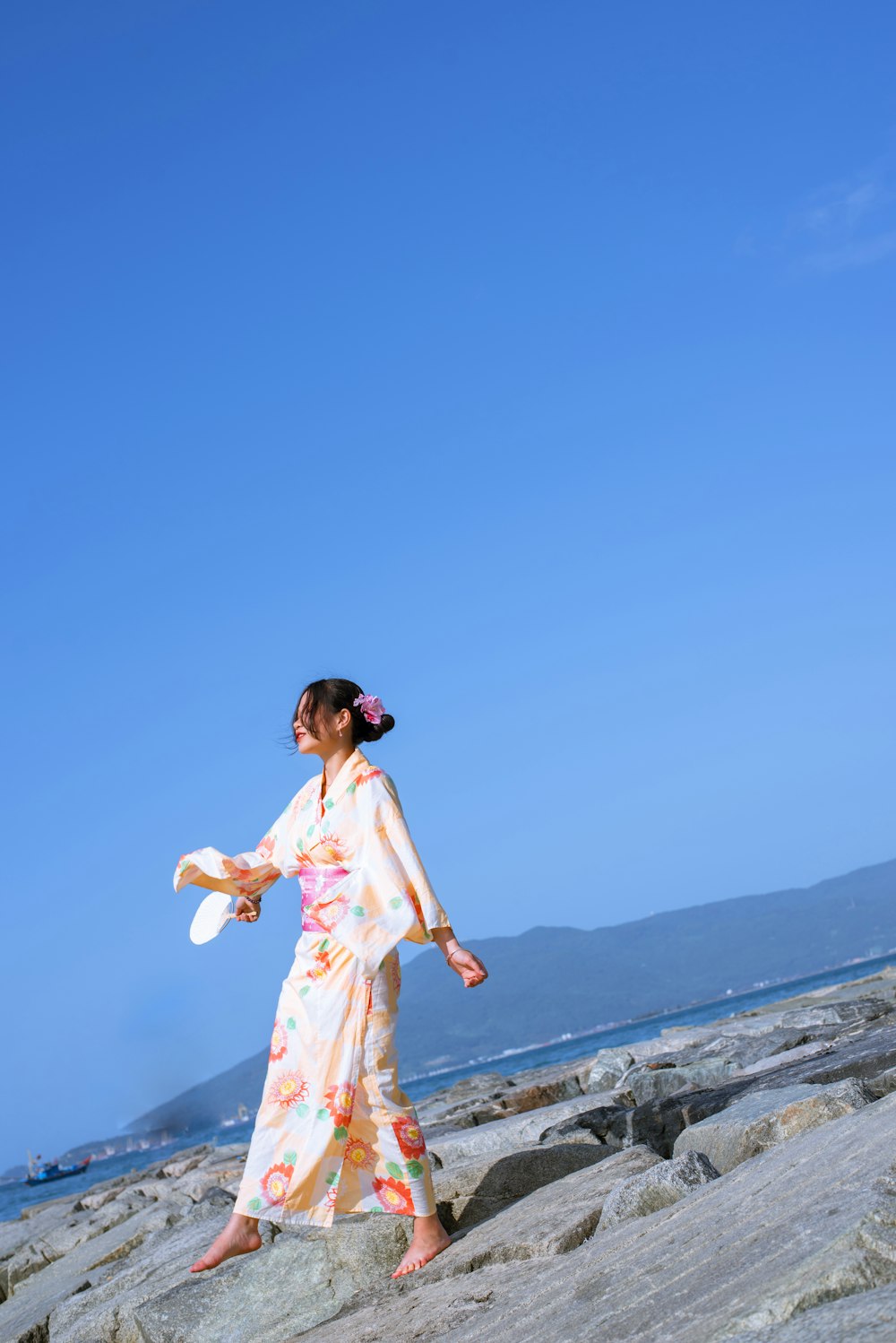 a woman in a kimono standing on rocks near the ocean