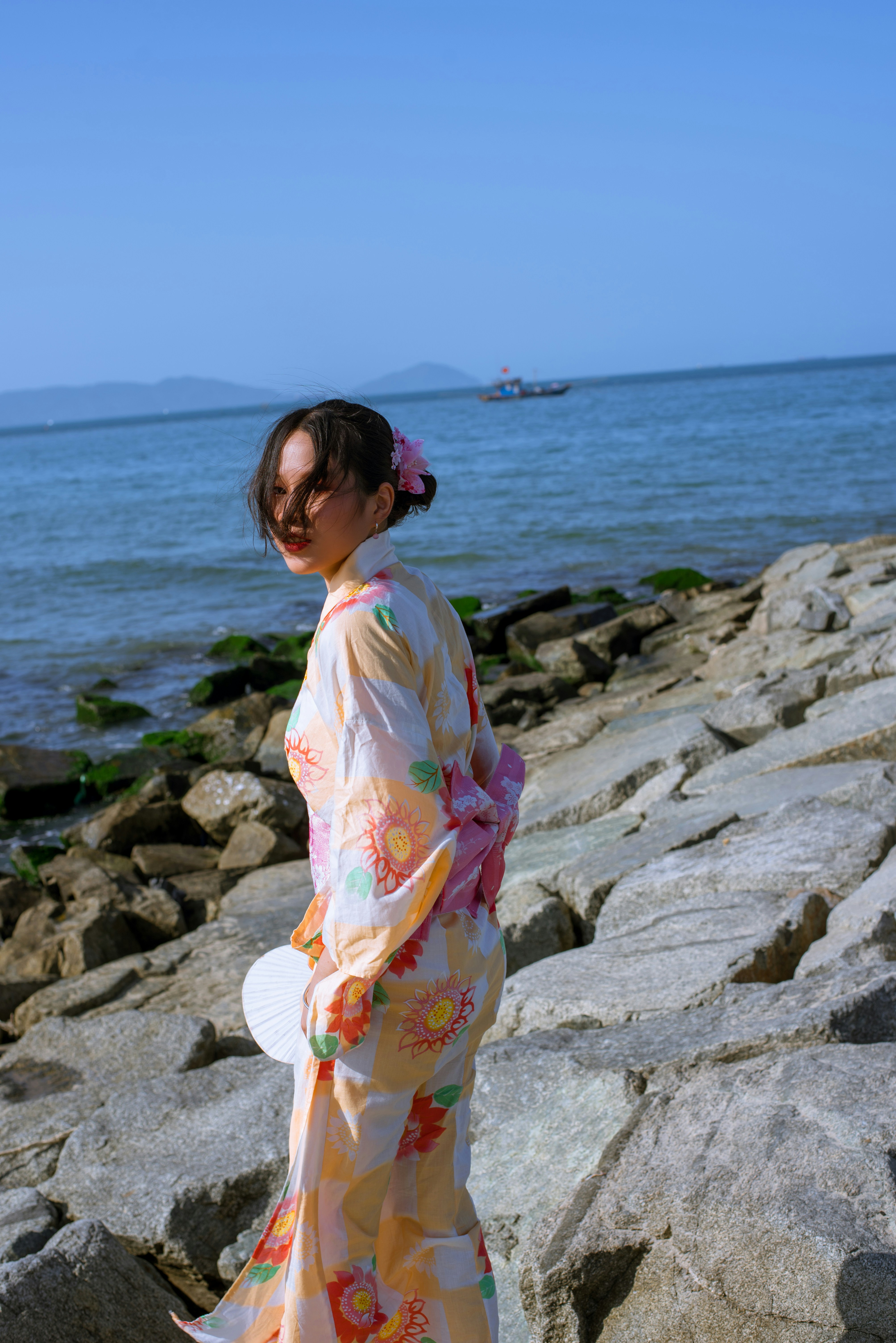 a woman in a kimono standing on rocks near the ocean
