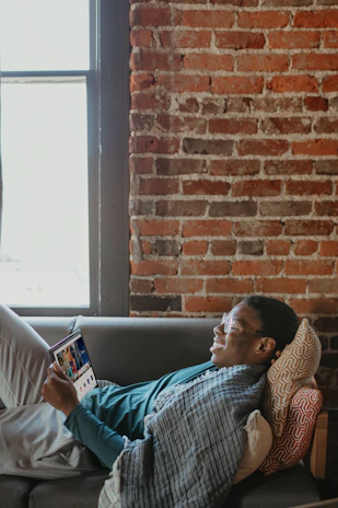 A user comfortably using an android app on a tablet while relaxing on a cozy couch.