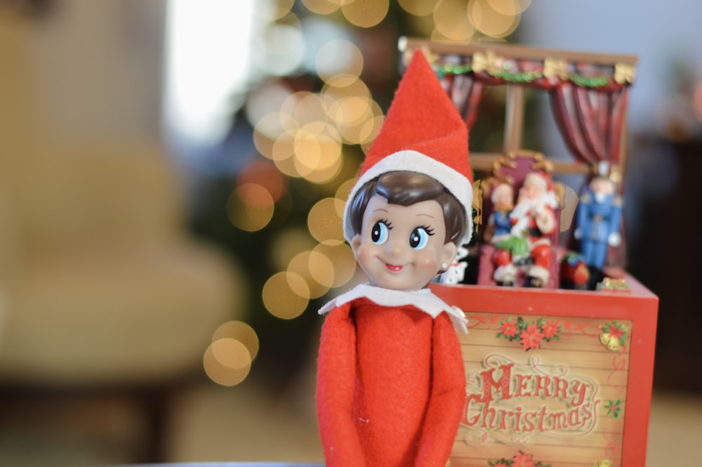 an elf doll sitting on top of a table next to a christmas box