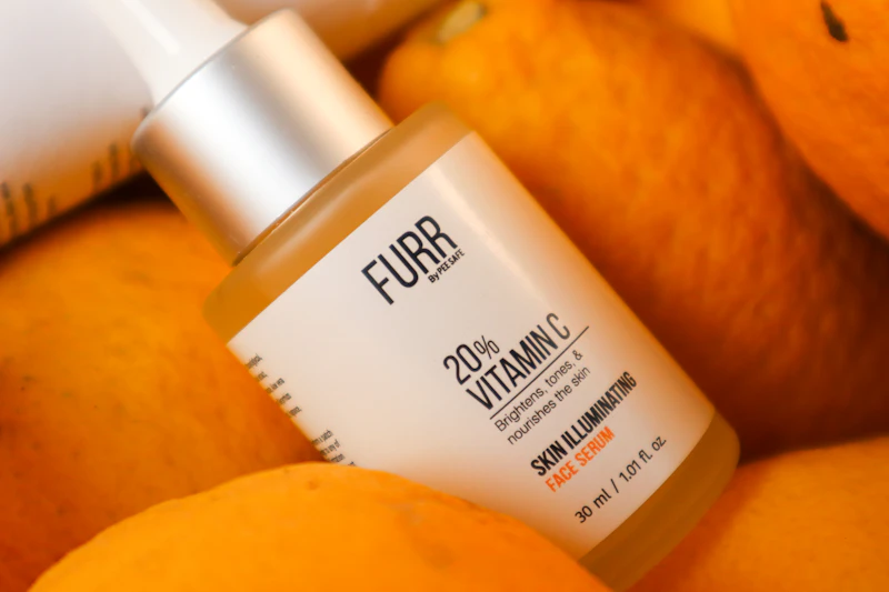 A vitamin C serum dropper bottle resting on fresh oranges