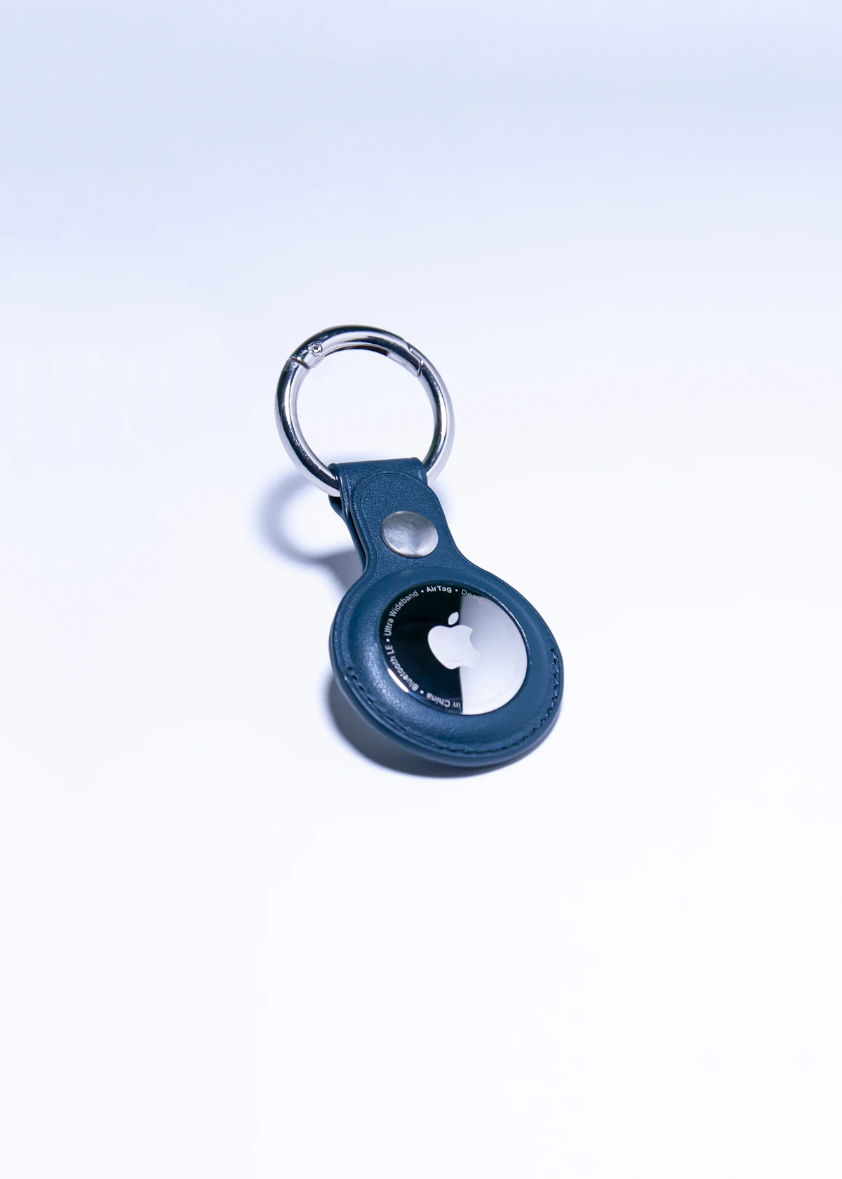 Apple AirTag in a blue leather keychain holder on a white surface, representing everyday use on house keys