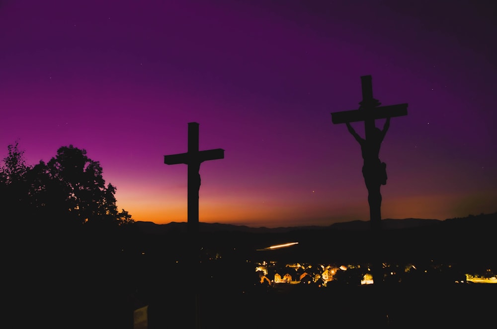 a cross and a crucifix are silhouetted against a purple sky
