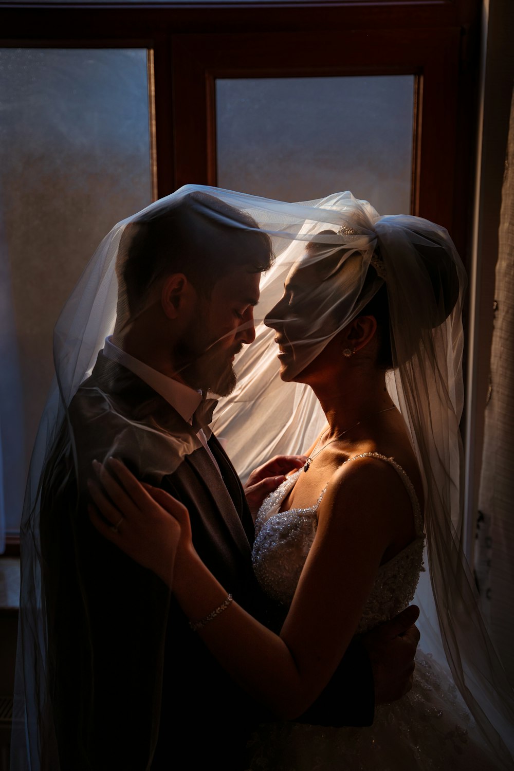 a bride and groom embracing in front of a window