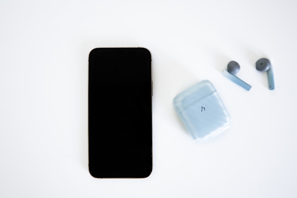 Un iPhone, des écouteurs et un étui sur une surface blanche