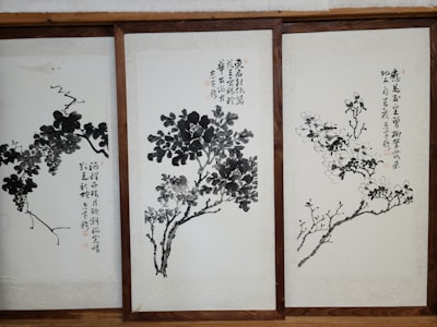 Three framed artworks feature traditional Chinese ink paintings depicting trees or plants with calligraphy accompanying each piece. The brushwork is expressive, with varying shades of black and gray creating depth and texture on the pale background.