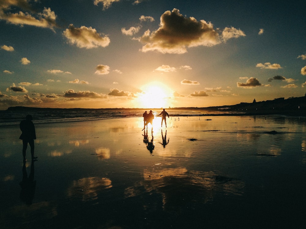 a group of people walking along a beach at sunset