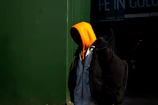 An orange hoodie with a simple design hanging against a dark backdrop.