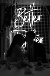 a man and woman kissing in front of a neon sign