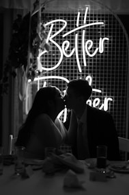 a man and woman kissing in front of a neon sign