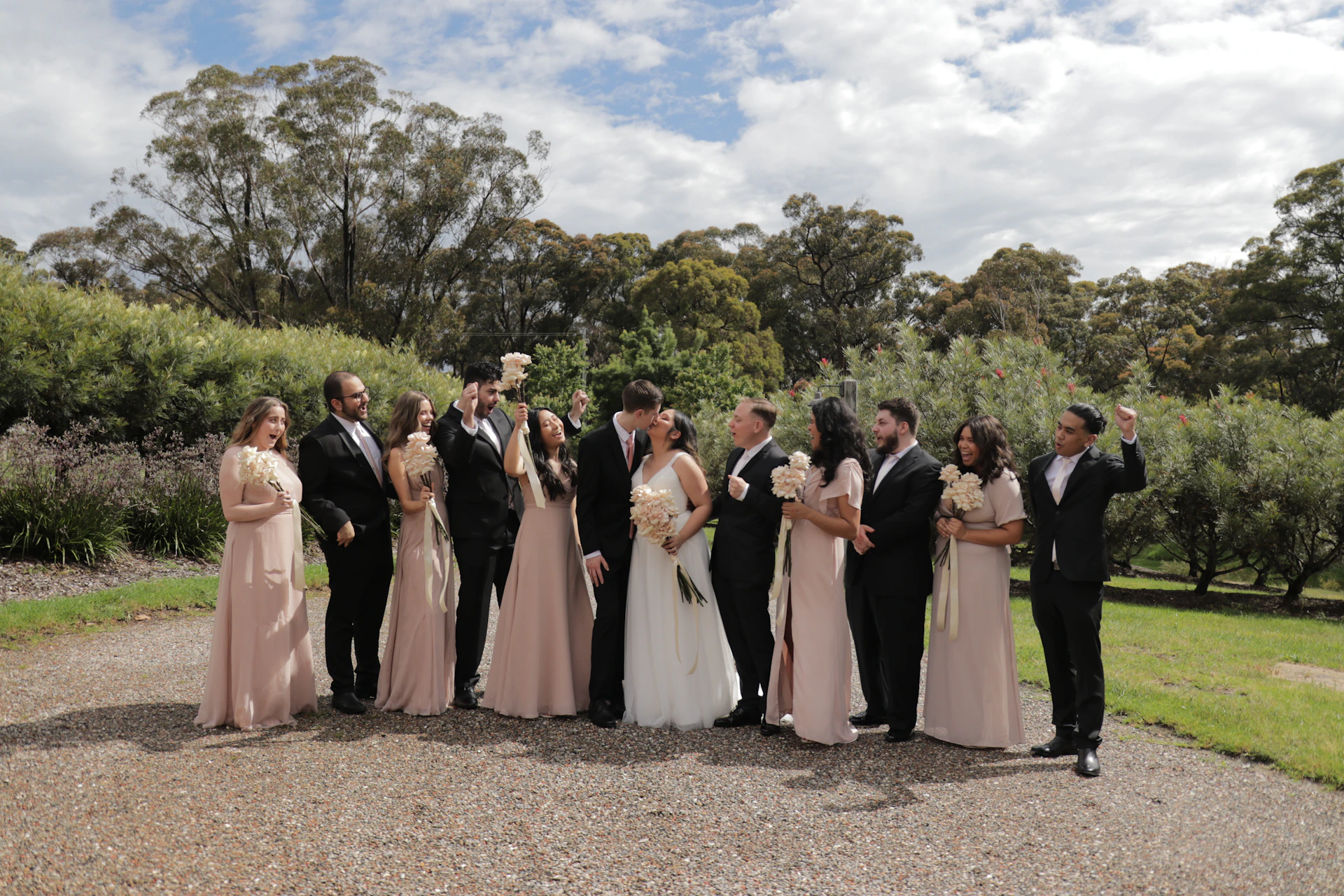 A candid shot of the wedding party laughing and celebrating outdoors, with natural greenery and tasteful decorations enhancing the festive atmosphere.