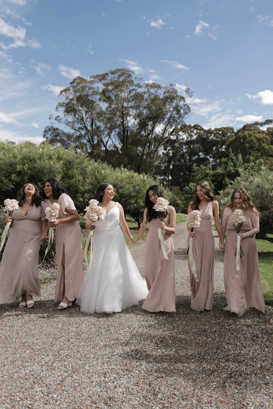 Bride walking outdoors with bridesmaids in blush dresses