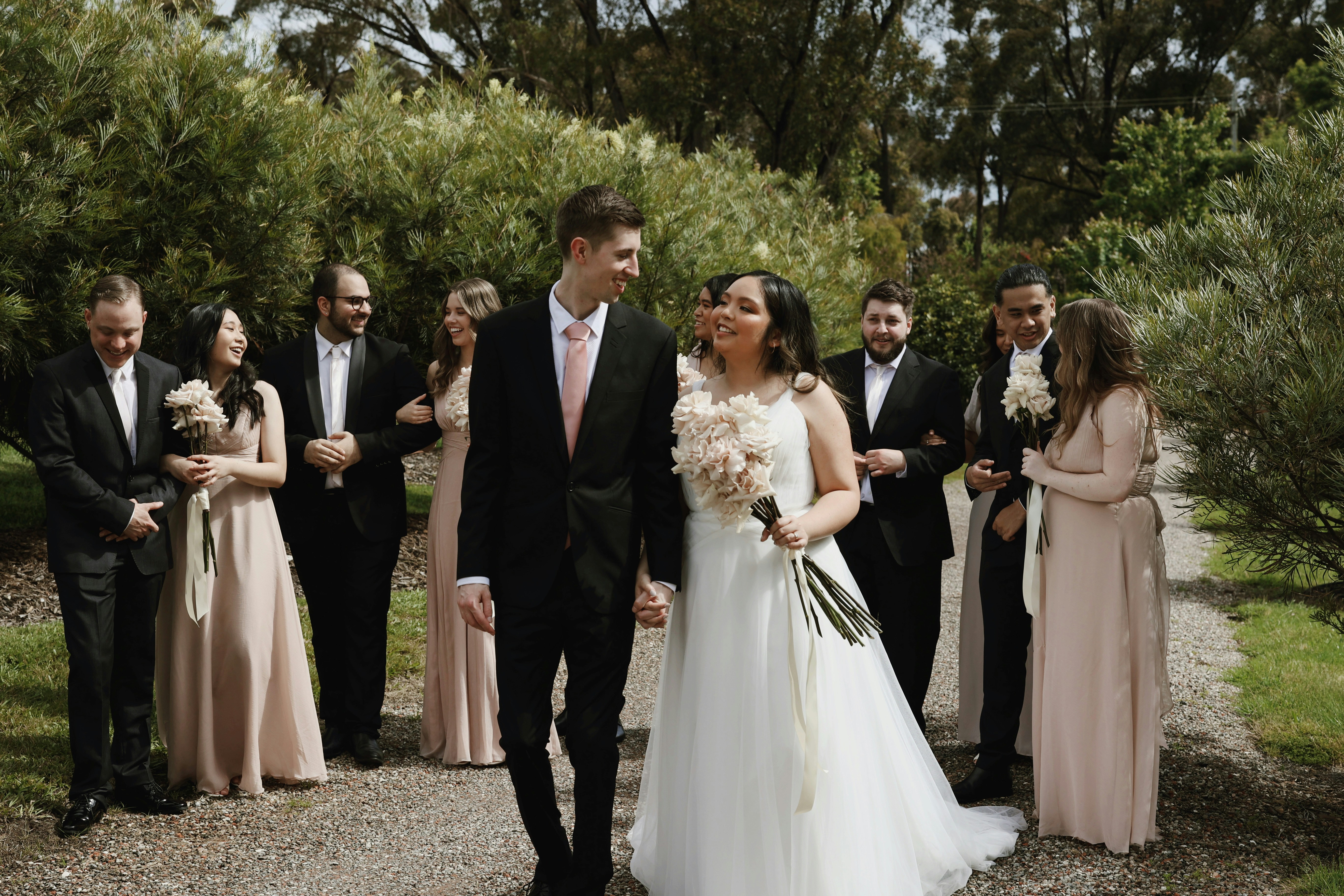 a bride and groom walking down a path with their wedding party