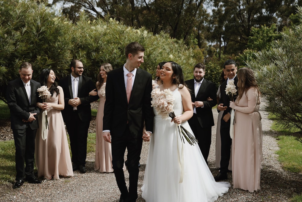 a bride and groom walking down a path with their wedding party