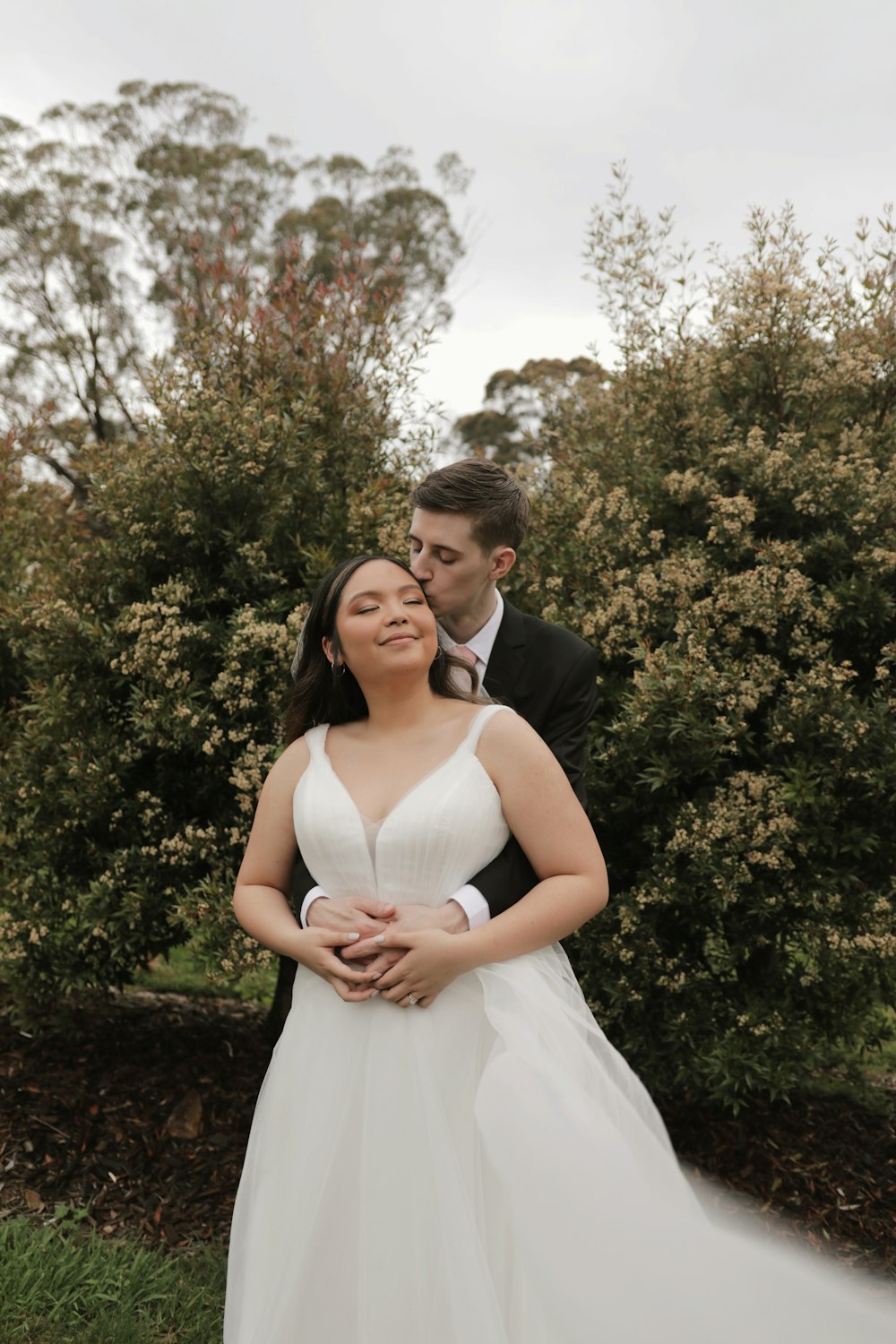 a bride and groom posing for a picture in front of some bushes