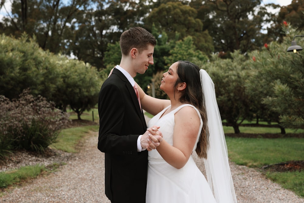 a bride and groom standing together in a park